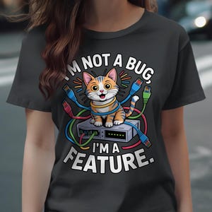 May include: Dark grey t-shirt with a cartoon cat in orange and white stripes on a network device. Text reads "I'M NOT A BUG, I'M A FEATURE." The cat and device are surrounded by colourful network cables.