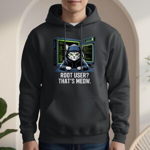 May include: Dark gray hoodie featuring a graphic of a cat in a hoodie, with computer screens in the background. The text reads "ROOT USER? THAT'S MEOW." The hoodie has a front pocket and a drawstring hood.