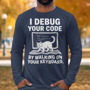 Puede incluir: Camiseta de manga larga azul marino con el texto "I Debug Your Code By Walking On Your Keyboard". El diseño presenta un gato blanco en una pantalla de ordenador. Ropa cómoda e informal.