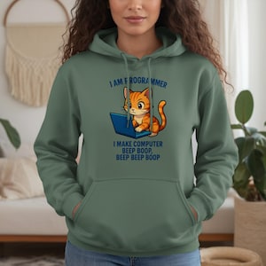 May include: A green hooded sweatshirt featuring a cartoon cat on a laptop. The cat is orange and white. Text on the sweatshirt reads "I AM FROGRAMMER" and "I MAKE COMPUTER BEEP BOOP, BEEP BEEP BOOP."