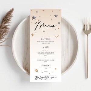May include: A baby shower menu card with a celestial theme. The menu features a soft beige background adorned with gold and gray stars and a crescent moon. The menu includes the word "Menu" and the words "Entree", "Main", and "Dessert".
