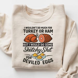 May include: Sand-colored sweatshirt with the text "I wouldn't do much for turkey or ham but I would do some sketchy shit for deviled eggs." The graphic includes illustrations of a roasted turkey, ham, and deviled eggs.