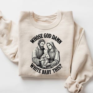 May include: Sand-colored sweatshirt with a graphic of a religious family and the text "Whose God Damn White Baby This?" The graphic is in black and white, and the sweatshirt has long sleeves.