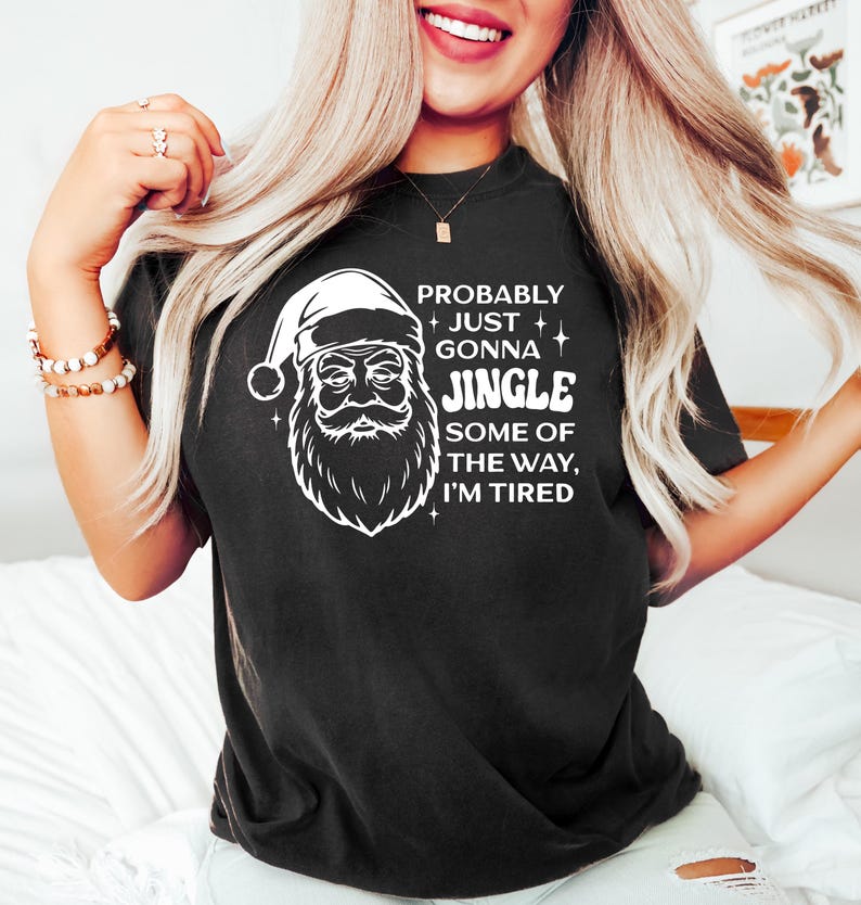 May include: Black t-shirt featuring a white graphic of Santa Claus with the text "Probably Just Gonna Jingle Some of the Way, I'm Tired." The shirt is a casual, comfortable style, perfect for the holiday season.