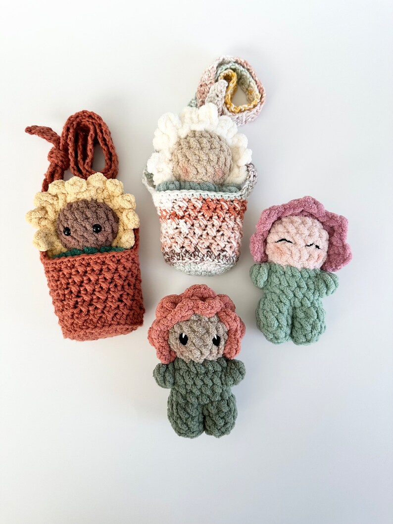 May include: Five crocheted flower-shaped plushies. Two are in flower pots, one is a sunflower, one is a pink flower, and one is a green flower.