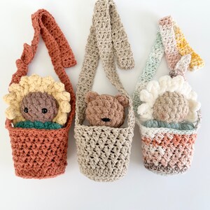 May include: Three crocheted bags with straps, each featuring a different crocheted animal inside. The bags are in shades of brown, beige, and pink. The animals are a sunflower, a bear, and a daisy.