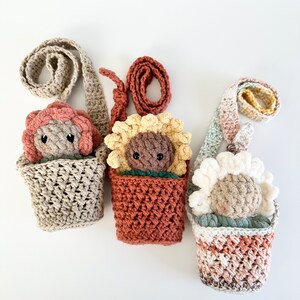 May include: Three crocheted flower-shaped plushies in different colors, each with a crocheted pot and a strap, hanging on a white background.