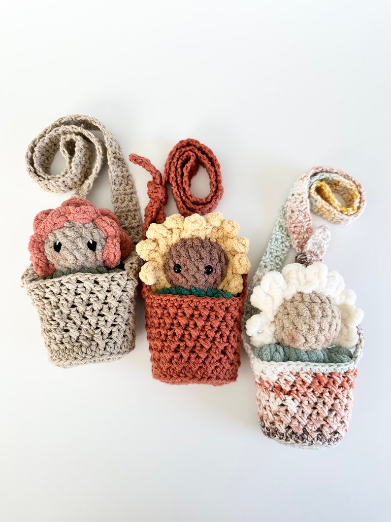 May include: Three crocheted flower-shaped plushies in different colors, each with a crocheted pot and a strap, hanging on a white background.