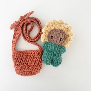 May include: A crocheted sunflower doll with a brown face and green body, and a crocheted orange bag with a long strap.