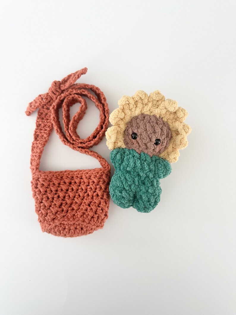 May include: A crocheted sunflower doll with a brown face and green body, and a crocheted orange bag with a long strap.