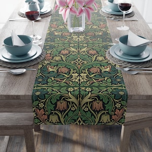 May include: A rectangular table runner featuring a dark green background with a repeating pattern of stylized flowers and leaves in shades of gold, orange, and green. The runner is centered on a wooden table set with blue bowls, wine glasses, and flowers.