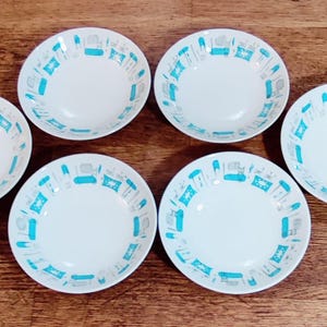 May include: Six white ceramic bowls with a turquoise and gray geometric pattern around the rim. The bowls are arranged on a wooden surface, showcasing a vintage or retro design. The bowls are suitable for serving soup or cereal.