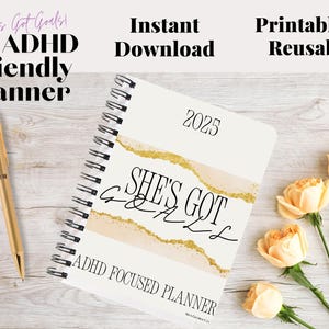Może przedstawiać: Planer przyjazny dla osób z ADHD z tekstem "She's Got Goals" i "ADHD Focused Planner". Spiralny planer jest otwarty na stronie z rokiem 2025. Złoty długopis leży obok planera, a brzoskwiniowe róże są w tle.