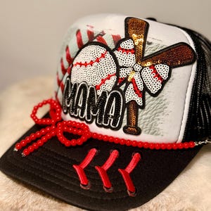 K&ouml;nnte beinhalten: Baseball-Trucker-Cap mit schwarzem Schirm und Mesh-R&uuml;cken. Auf der Vorderseite befinden sich ein Baseball, ein Schl&auml;ger und das Wort "MAMA" in Pailletten. Eine rote Perlen-Schleife und -N&auml;hte verleihen diesem sportlichen Accessoire Details.