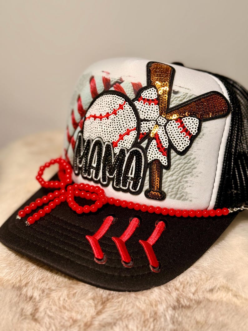 K&ouml;nnte beinhalten: Baseball-Trucker-Cap mit schwarzem Schirm und Mesh-R&uuml;cken. Auf der Vorderseite befinden sich ein Baseball, ein Schl&auml;ger und das Wort "MAMA" in Pailletten. Eine rote Perlen-Schleife und -N&auml;hte verleihen diesem sportlichen Accessoire Details.