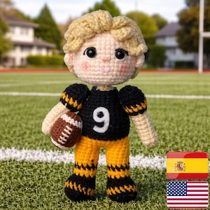 Könnte beinhalten: Handgemachte Häkelpuppe eines Footballspielers, der ein schwarzes Trikot mit der Nummer 9 und gelbe Hosen trägt. Die Puppe hat blondes Haar und hält einen braunen und weißen Football. Die Puppe steht auf einem grünen Feld.
