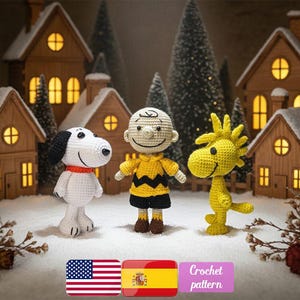 May include: Crocheted figures of Snoopy, Charlie Brown, and Woodstock stand in a snowy scene with miniature houses and trees. The figures are in white, yellow, and black. The image includes the text "Crochet pattern" and the flags of the United States and Spain.