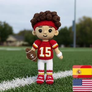 May include: Crocheted doll of a football player in a red jersey with the number 15, white pants, and red shoes. The doll has brown hair, a red headband, and is holding a brown football. The doll is standing on green grass.