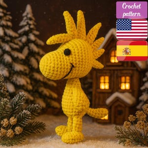 May include: A handmade yellow crochet bird with a black eye and a smiling face. The bird is standing in front of a miniature house and snowy evergreen trees. The image includes the text "Crochet pattern", the American flag, and the Spanish flag.