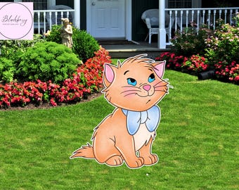 Op de afbeelding: Een cartoonafbeelding van een oranje kat met blauwe ogen en een blauwe vlinderdas, zittend op groen gras. De kat is een uitsparing, waarschijnlijk voor buitendecoratie. De achtergrond omvat een huis, bloemen en groen.