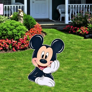 May include: A large, colorful cutout of Mickey Mouse, with a black body, white gloves, and a smiling face. The cutout is placed on a green lawn, with a garden and house in the background. The character is leaning on his hand.