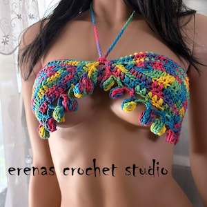 Puede incluir: Un top de bikini de crochet colorido con un estilo halter y pompones a lo largo del borde inferior. El top está hecho con una variedad de colores, incluyendo rosa, amarillo, verde, azul y morado. El texto "erenas crochet studio" es visible en la parte inferior de la imagen.