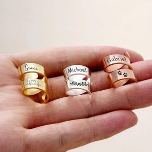 Pu&ograve; includere: Tre anelli avvolgenti personalizzati in oro, argento e oro rosa. L'anello d'oro &egrave; inciso con "Grace" e una linea del battito cardiaco. L'anello d'argento dice "Michael" con un disegno a foglie. L'anello in oro rosa dice "Gabriel" e ha impronte di zampe.