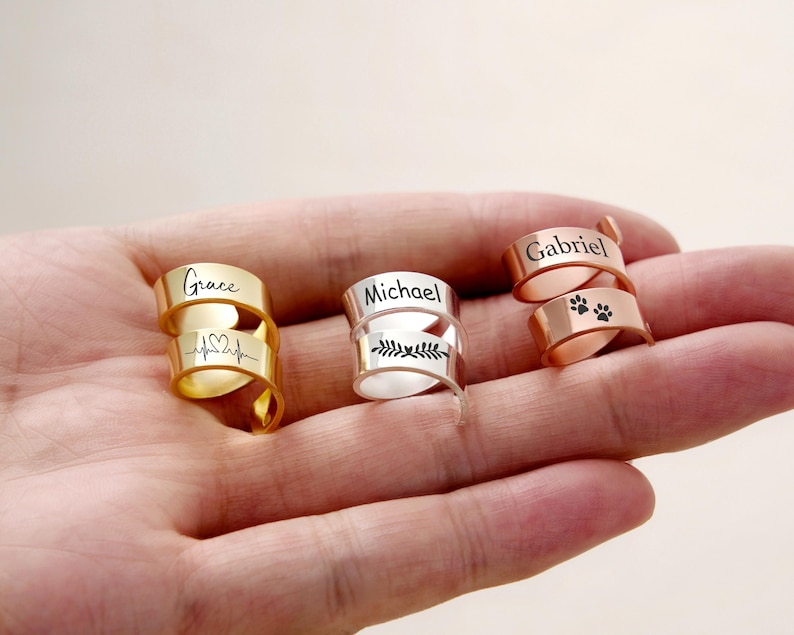 Pu&ograve; includere: Tre anelli avvolgenti personalizzati in oro, argento e oro rosa. L'anello d'oro &egrave; inciso con "Grace" e una linea del battito cardiaco. L'anello d'argento dice "Michael" con un disegno a foglie. L'anello in oro rosa dice "Gabriel" e ha impronte di zampe.