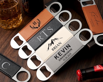 May include: A collection of personalized bottle openers with leather-like handles in various colors, including brown, black, cream, and gray. Each opener features a silver-colored bottle opener and is engraved with initials, names, or dates. The openers are arranged on a wooden surface.