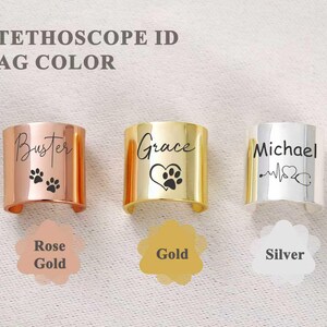 Pu&ograve; includere: Tre targhette identificative per stetoscopio in oro rosa, oro e argento. Il tag in oro rosa dice "Buster" con impronte di zampe. Il tag dorato dice "Grace" con un cuore e un'impronta di zampa. Il tag argentato dice "Michael" con un battito cardiaco e uno stetoscopio.