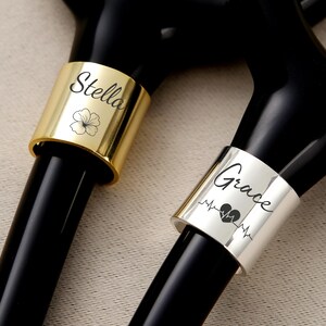 Pu&ograve; includere: Primo piano di due stetoscopi con anelli personalizzati. Un anello &egrave; dorato con il nome "Stella" e un fiore, l'altro &egrave; argentato con il nome "Grace", un cuore e una linea del battito cardiaco.