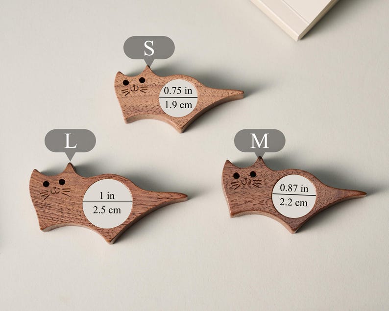 May include: Three wooden cat-shaped items in varying sizes. The smallest is 0.75 inches (1.9 cm) wide, the medium is 0.87 inches (2.2 cm) wide, and the largest is 1 inch (2.5 cm) wide. Each has a carved face.
