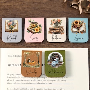 May include: A collection of six decorative magnetic bookmarks. Each bookmark features a unique design, including floral arrangements, a teacup, and illustrations of people reading. Names like "Rachel," "Casey," and "Gina" are written on the bookmarks.
