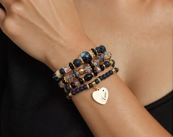 May include: A stack of beaded bracelets in shades of black, gold, and clear. The bracelets feature various bead sizes and textures, including a gold heart charm with the name "Karen" engraved on it. The bracelets are worn on a wrist.