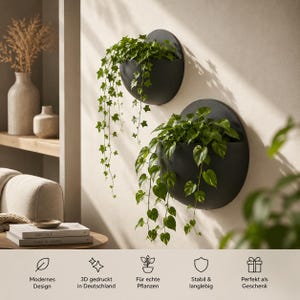 May include: Two matte black, semi-circular wall-mounted planters holding trailing green ivy and pothos plants. The planters feature a flat back and a curved front, mounted on a light-colored wall. Text at the bottom includes Modernes Design, 3D gedruckt in Deutschland, F&uuml;r echte Pflanzen, Stabil & langlebig, and Perfekt als Geschenk.