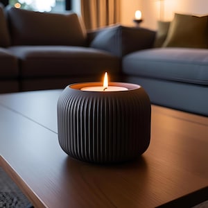 May include: A lit candle in a dark brown, ribbed ceramic holder. The candle has a white wax base and a small, flickering flame. The holder sits on a wooden table, with a blurred background of a living room.