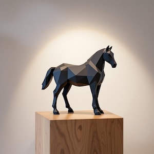 Op de afbeelding: Een zwarte geometrische paardensculptuur met een facetontwerp. Het paard staat op een houten kubus, met licht van bovenaf. De sculptuur heeft een moderne, minimalistische uitstraling.