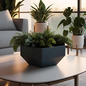 Puede incluir: Una escena de salón moderno con una jardinera gris oscuro llena de exuberantes helechos verdes y otras plantas. La jardinera está sobre una mesa de centro blanca. Otras plantas en macetas son visibles en el fondo, cerca de una ventana grande.