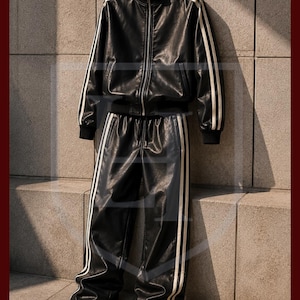 Peut inclure: Ensemble de surv&ecirc;tement en cuir noir avec des rayures blanches. La veste a une fermeture &eacute;clair sur le devant et un col et des poignets c&ocirc;tel&eacute;s. Le pantalon est large avec une taille &agrave; cordon. L'ensemble est contre un mur textur&eacute;.