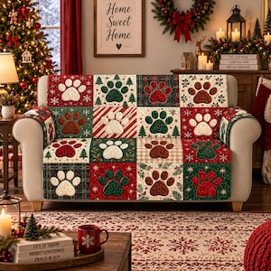 May include: A quilted sofa cover featuring a patchwork design of red, green, and white squares. Each square displays a stitched paw print motif, with alternating patterns of Christmas trees, snowflakes, plaid, and stripes throughout the fabric.