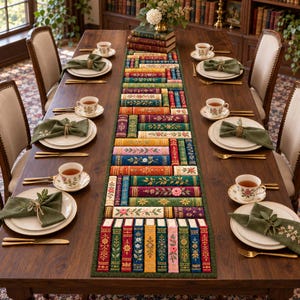 Puede incluir: Un camino de mesa rectangular largo con un patrón bordado de libros apilados con motivos florales, centrado en una mesa de comedor de madera oscura con platos blancos, tazas de té florales, servilletas verde oliva y cubiertos dorados.