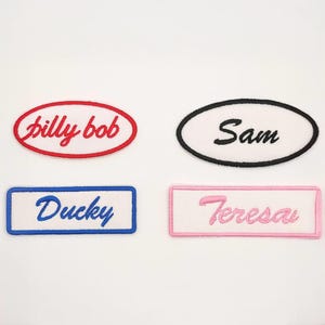 May include: Four embroidered name patches. Two are oval-shaped with the names "billy bob" in red and "Sam" in black. The other two are rectangular with the names "Ducky" in blue and "Teresa" in pink.
