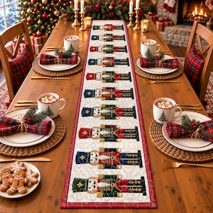 May include: A long rectangular table runner featuring a repeating pattern of nutcracker figures in red, blue, and green uniforms on a cream background, centered on a wooden dining table set with white mugs, plaid napkins, and gingerbread cookies.