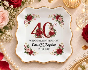Könnte beinhalten: Eine quadratische weiße Keramikschale mit gewelltem Goldrand, verziert mit roten Blumenmotiven, dem Text 40th WEDDING ANNIVERSARY, den Namen David und Sophia mit einem Herzsymbol sowie dem Datum 09.10.1986 in schwarzer Schrift.