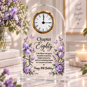 May include: An arched clear acrylic plaque featuring a gold-rimmed analog clock with Roman numerals. The plaque displays the text Chapter Eighty, the name Sophia, and a birthday message surrounded by printed purple iris flowers and small butterflies.
