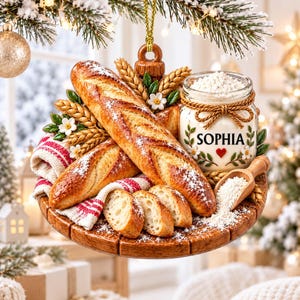 Può includere: Un ornamento rotondo con texture effetto legno che presenta due baguette dorate, tre fette di pane, un barattolo di vetro riempito di farina bianca con l'etichetta SOPHIA e un cuore rosso, spighe di grano, fiori bianchi e un piccolo cucchiaio in legno.