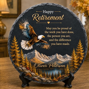 Puede incluir: Una placa redonda de pizarra negra con un águila calva en vuelo, un paisaje montañoso con árboles dorados y el texto: Happy Retirement, May you be proud of the work you have done, the person you are, and the difference you have made. Oliver Peterson.