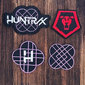 Könnte beinhalten: Vier gestickte Aufnäher mit einzigartigen Designs. Ein Aufnäher zeigt das Wort "HUNTRIX" in Weiß mit einem geometrischen Design. Ein weiterer ist ein rotes und schwarzes Schild mit einem Löwen. Die anderen beiden Aufnäher haben geometrische Designs in Schwarz und Lila.