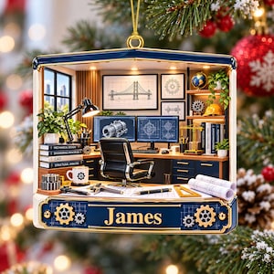 May include: A rectangular Christmas ornament featuring a detailed miniature engineering office scene with a desk, computer monitors, a black chair, and blueprints. The blue frame displays the name James and gear motifs, hanging from a gold loop.