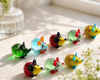 May include: A collection of seven small, handcrafted glass animal figurines shaped like hedgehogs or mice. Each piece features a distinct color combination, including red, yellow, green, and blue, with smooth, glossy surfaces and pointed snouts.